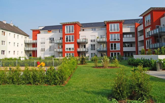 Wohnanlage mit rot-weißen Häusern, gruppiert um eine Rasenfläche mit Sträuchern und Spielplatz